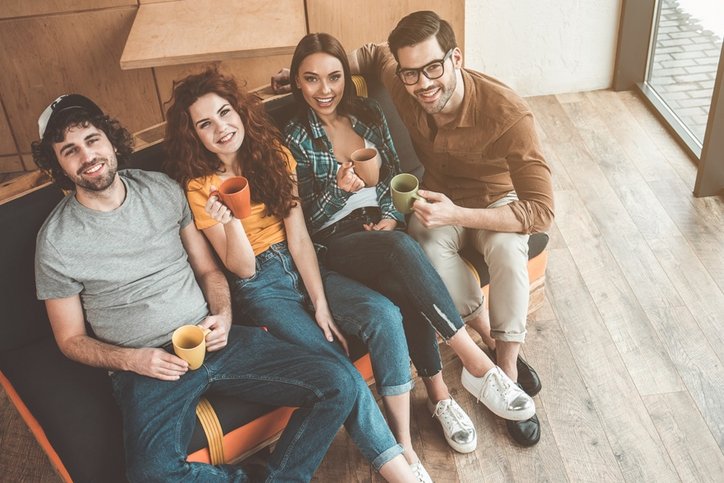 Draufsicht auf fröhliche junge Männer und Frauen, die Tee trinken und auf dem Sofa sitzen. © AdobeStock_ Yakobchuk Olena