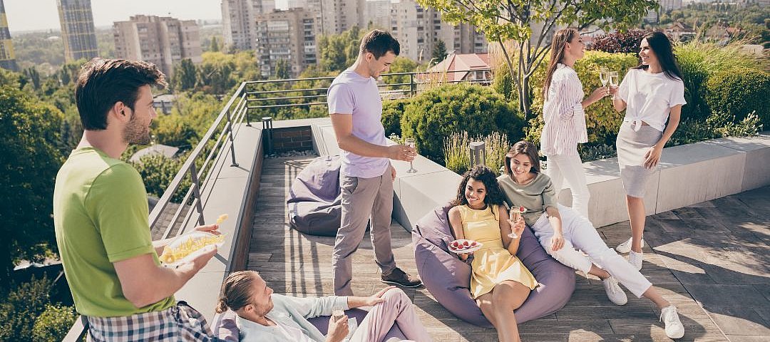 Geschäftsreisende und immer mehr Freizeitreisende haben sich in diesem Jahr wieder auf den Weg gemacht und checken vermehrt in Serviced Apartments ein. © stock.adobe.com_deagreez Eine Gruppe junger Leute entspannt auf einer Dachterrasse.