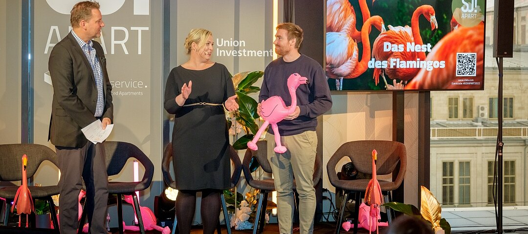 „Herzlichen Glückwunsch, Happyhotel“, hieß es 2022 durch die Moderatoren Anett Gregorius und Kai Böcking (l.). Die Jury hatte das „Nest des Flamingos“ an den Co-Founder Rafael Weißmüller (r.) des Revenue-Management-Software-Unternehmens verge