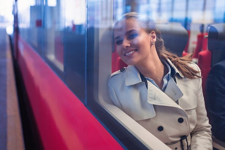 Eine Frau schaut lächelnd aus einem fahrenden Zug. © stock.adobe.com_AboutLife