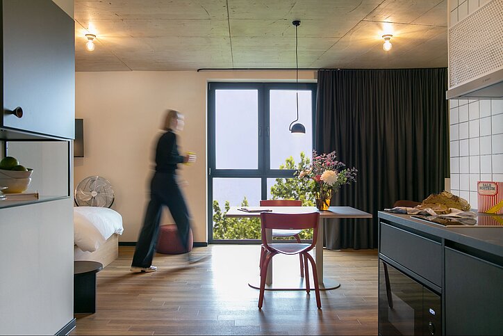 Apartment mit Fenster, Tisch, Küchenzeile und einer Person, die durchläuft
