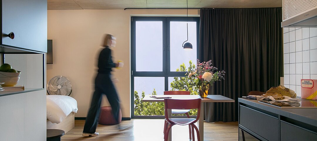 Apartment mit Fenster, Tisch, Küchenzeile und einer Person, die durchläuft