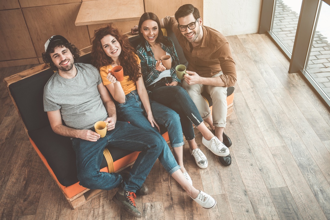 Draufsicht auf fröhliche junge Männer und Frauen, die Tee trinken und auf dem Sofa sitzen. © AdobeStock_ Yakobchuk Olena